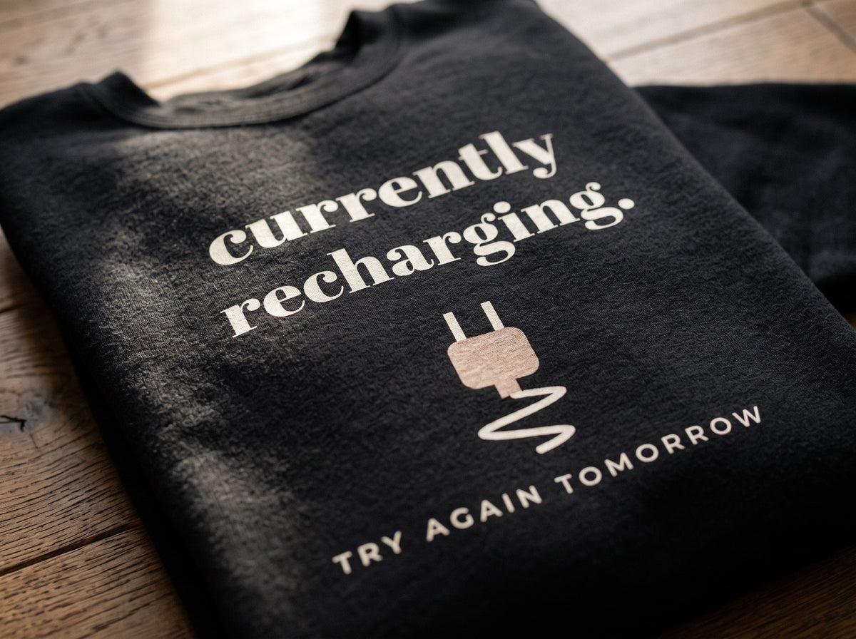 Currently Recharging Crewneck, the print up close on black fleece: currently recharging, a plug and TRY AGAIN TOMORROW.