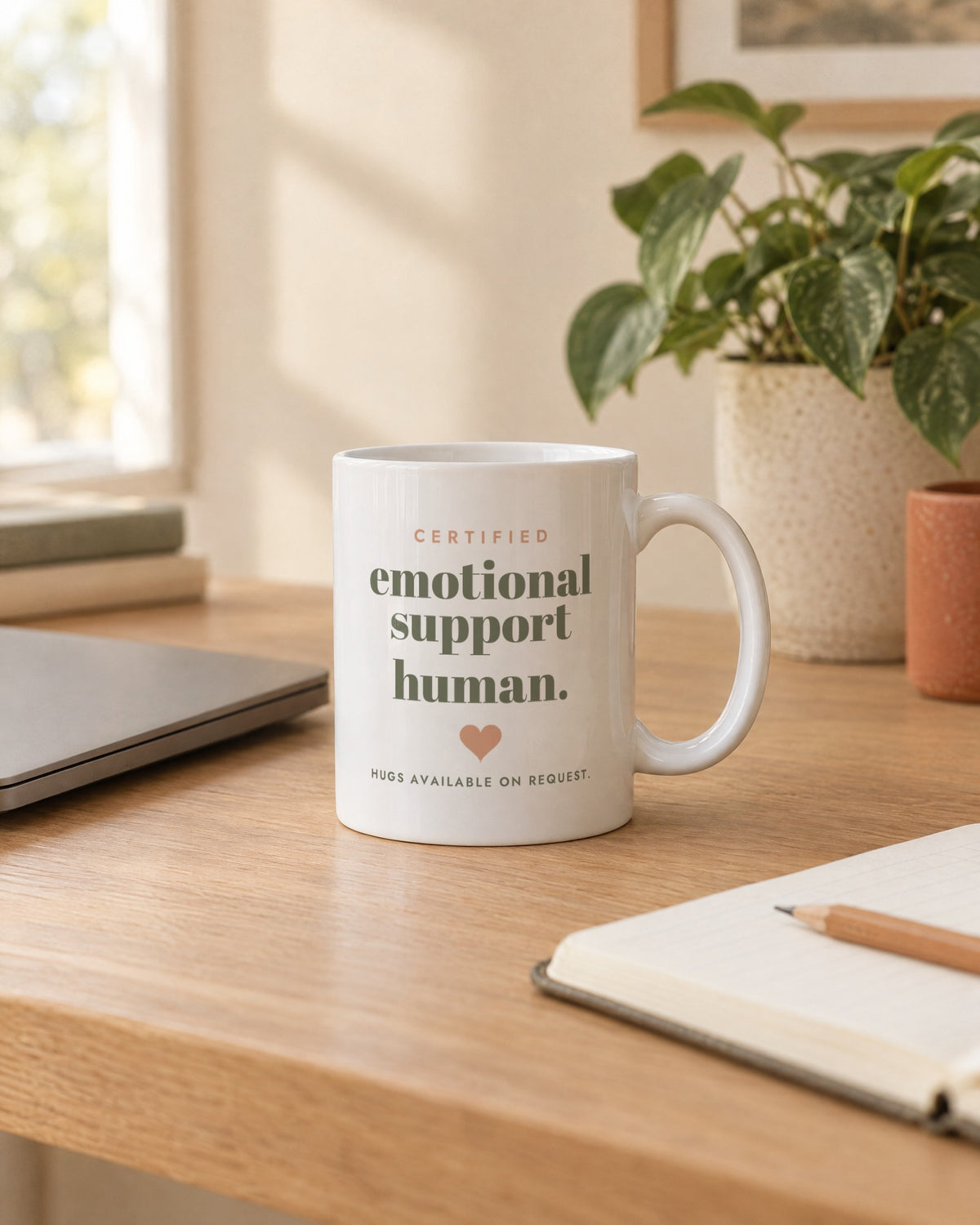 Emotional Support Human Mug, white ceramic 11 oz, on a desk next to a laptop