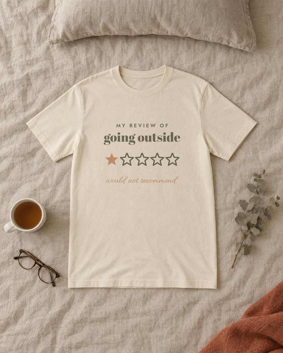 Going Outside, One Star Tee, in soft cream, laid flat on a made bed