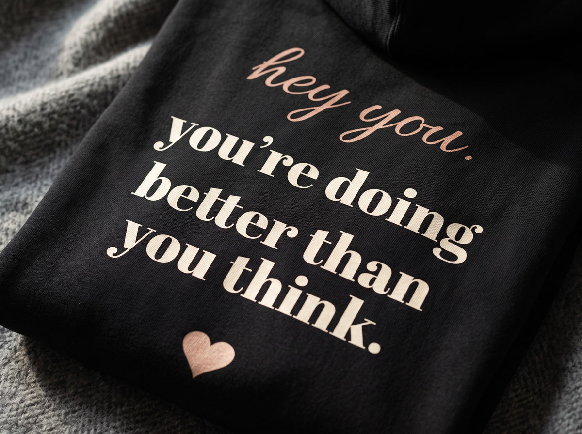 Hey You Hoodie, the back print up close on black fleece: "hey you. you're doing better than you think." and a small heart.