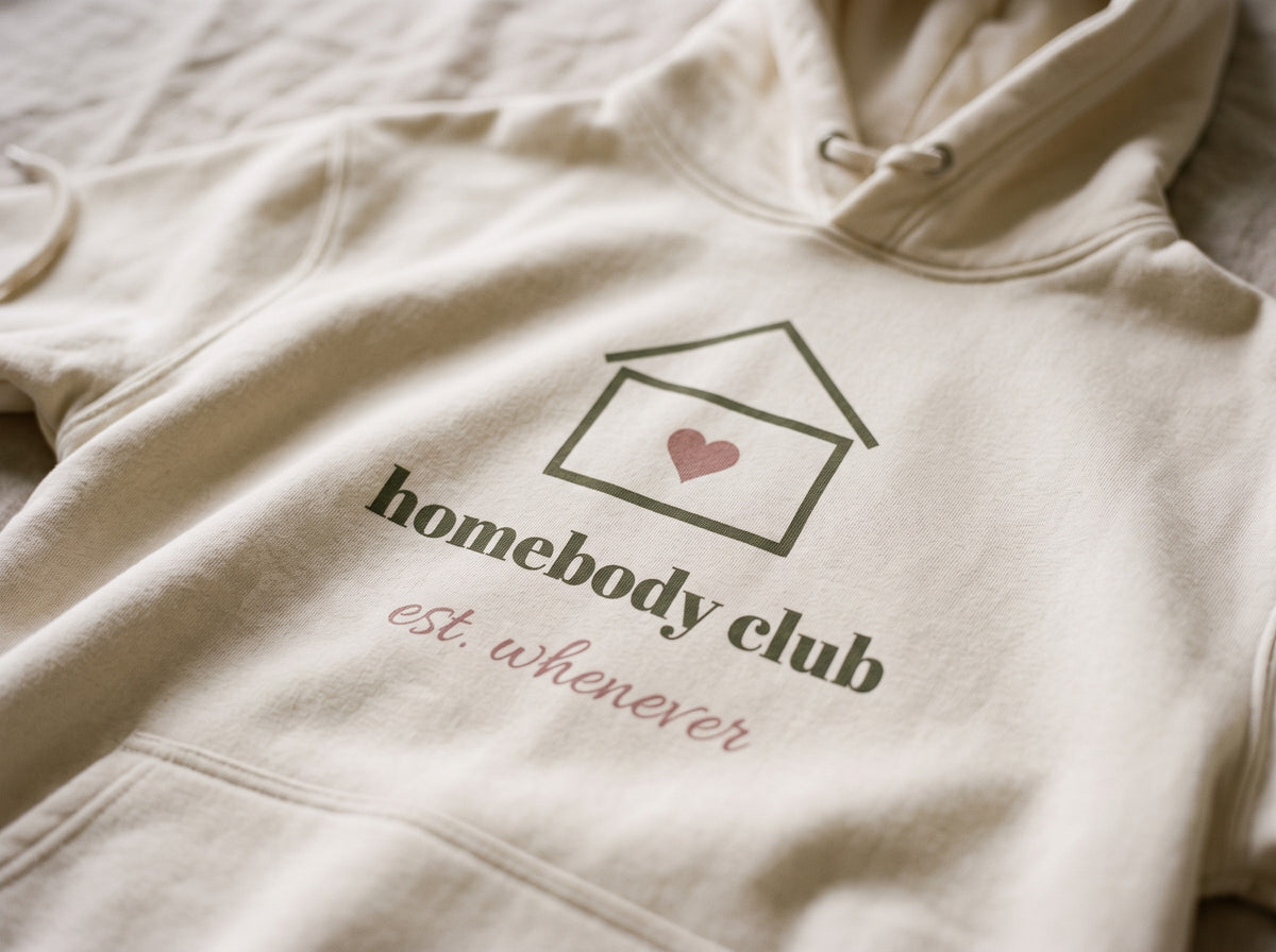 Homebody Club Hoodie, the print up close on Bone fleece: a small house with a heart, homebody club and est. whenever.