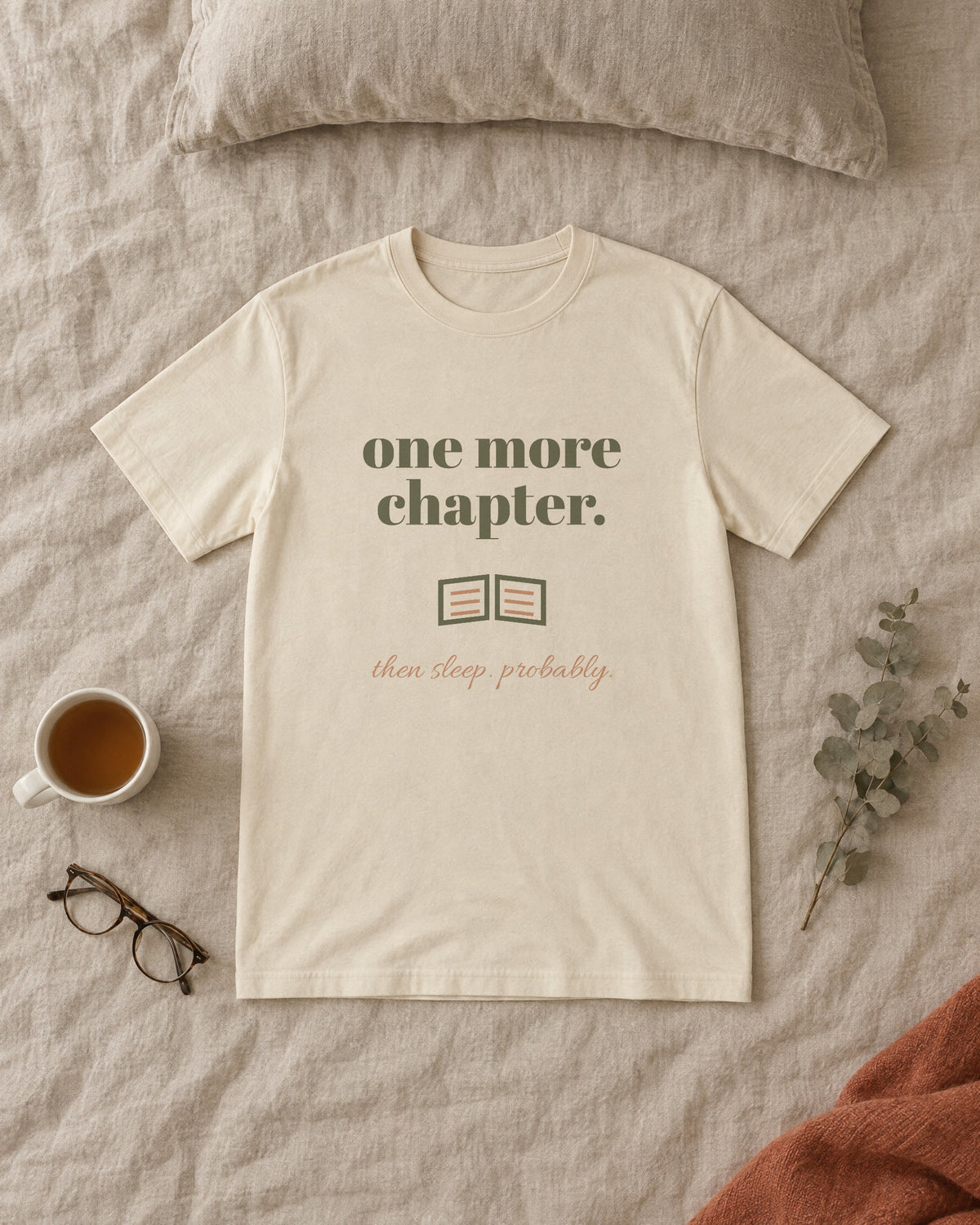 One More Chapter Tee, in soft cream, laid flat on a made bed