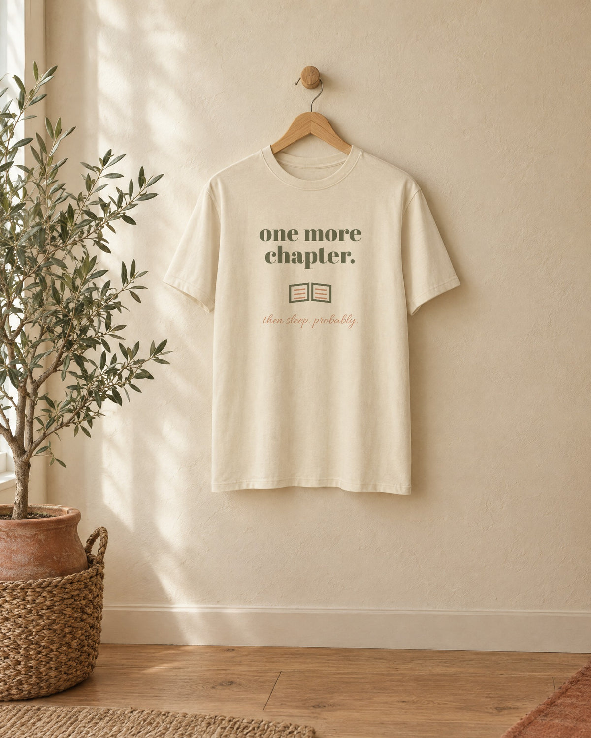 One More Chapter Tee, in soft cream, on a wooden hanger against a cream wall