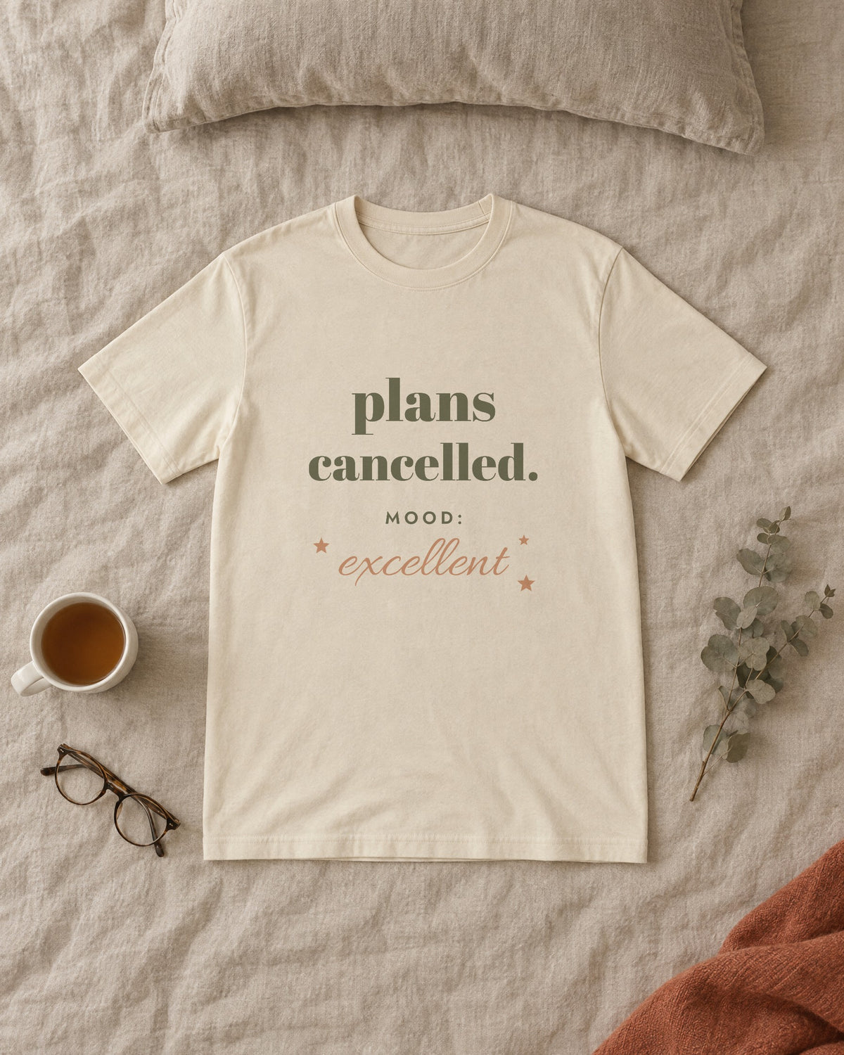 Plans Cancelled Tee, in soft cream, laid flat on a made bed