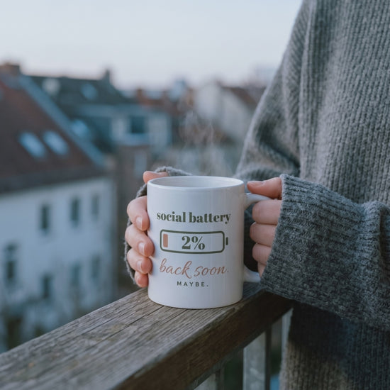 Social Battery Mug, a short clip of warm hands around the mug on a balcony at dawn