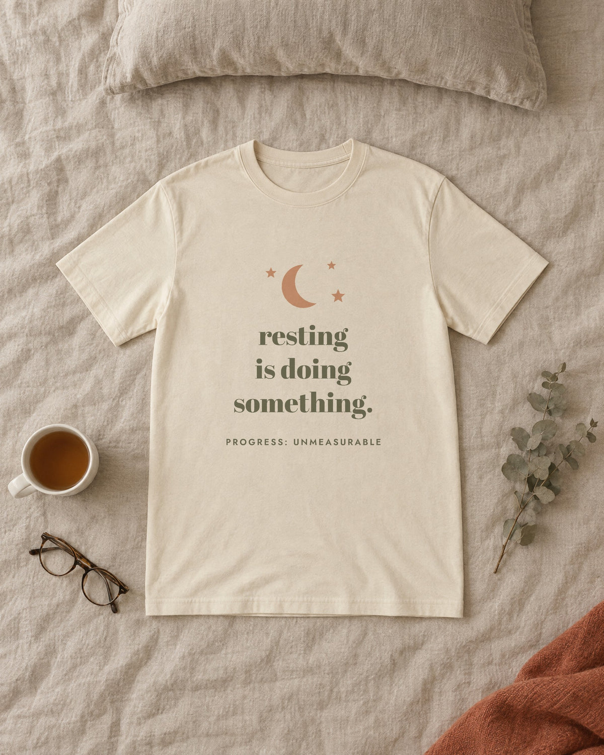 Resting Is Doing Something Tee, in soft cream, laid flat on a made bed