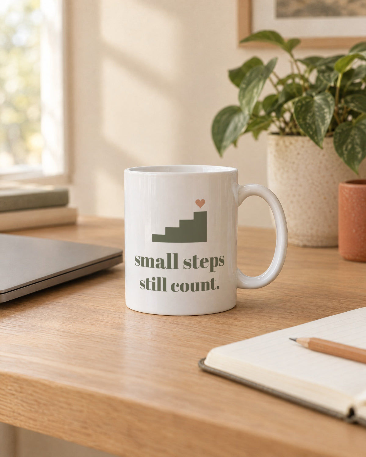 Small Steps Still Count Mug, white ceramic 11 oz, on a desk next to a laptop