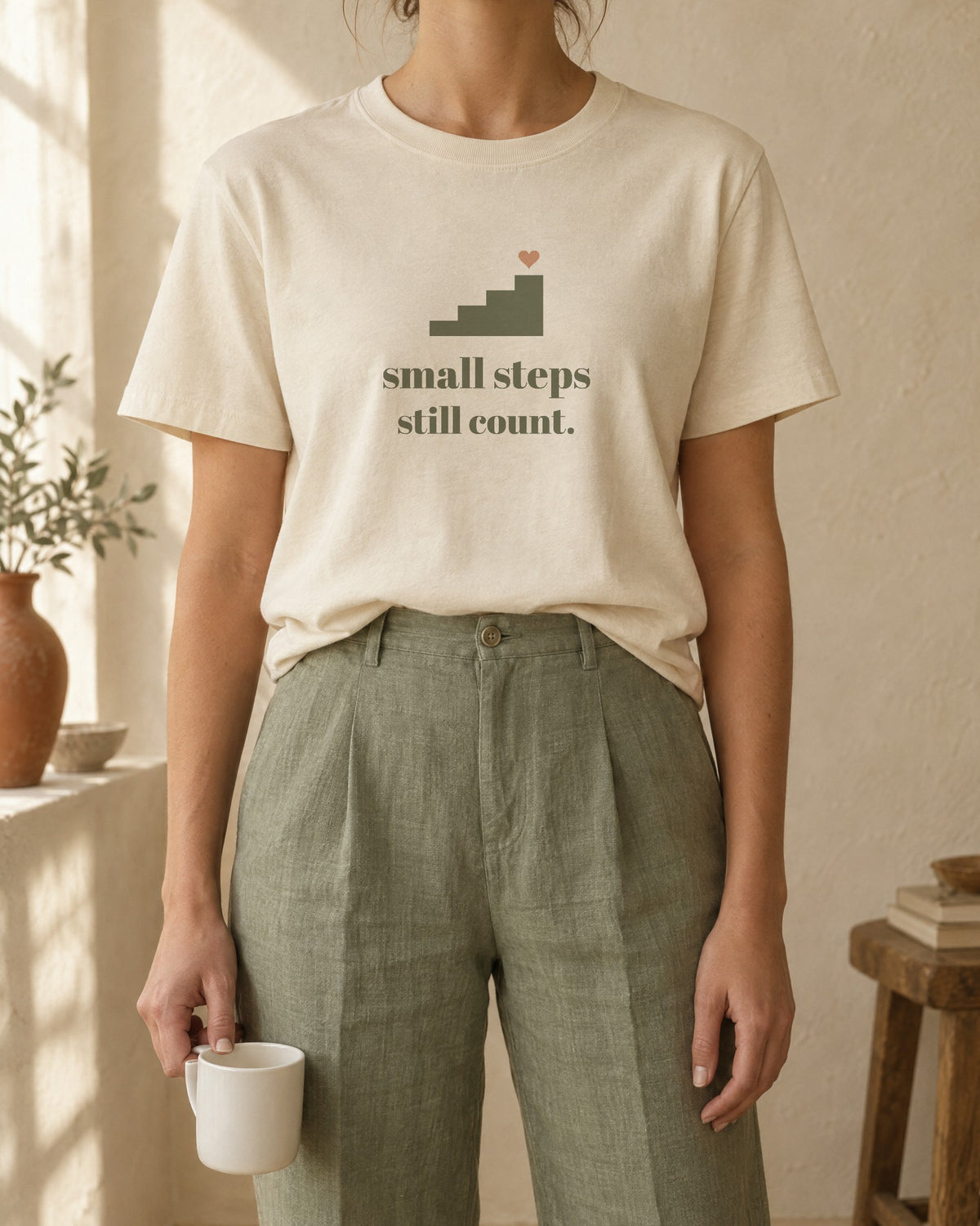 Small Steps Still Count Tee, in soft cream, worn with sage linen trousers
