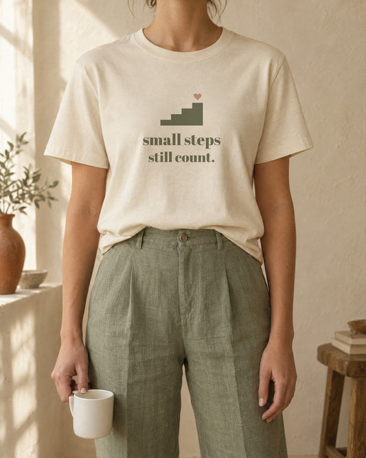 Small Steps Still Count Tee, in soft cream, worn with sage linen trousers