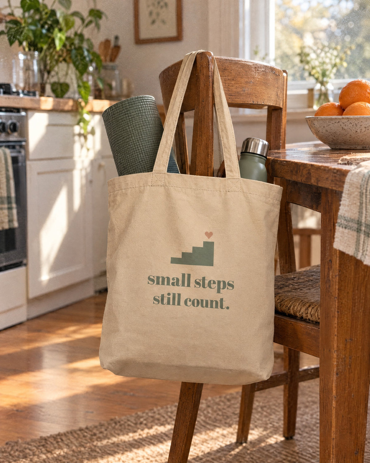 Small Steps Still Count Tote, hanging on a kitchen chair with a yoga mat