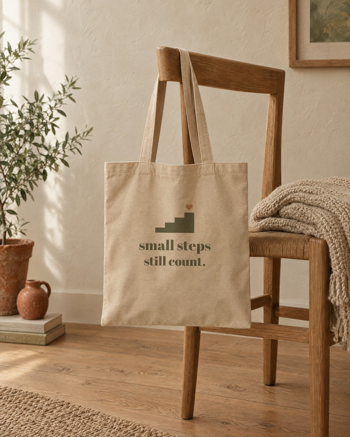Small Steps Still Count Tote, in natural oyster, hanging on a wooden chair