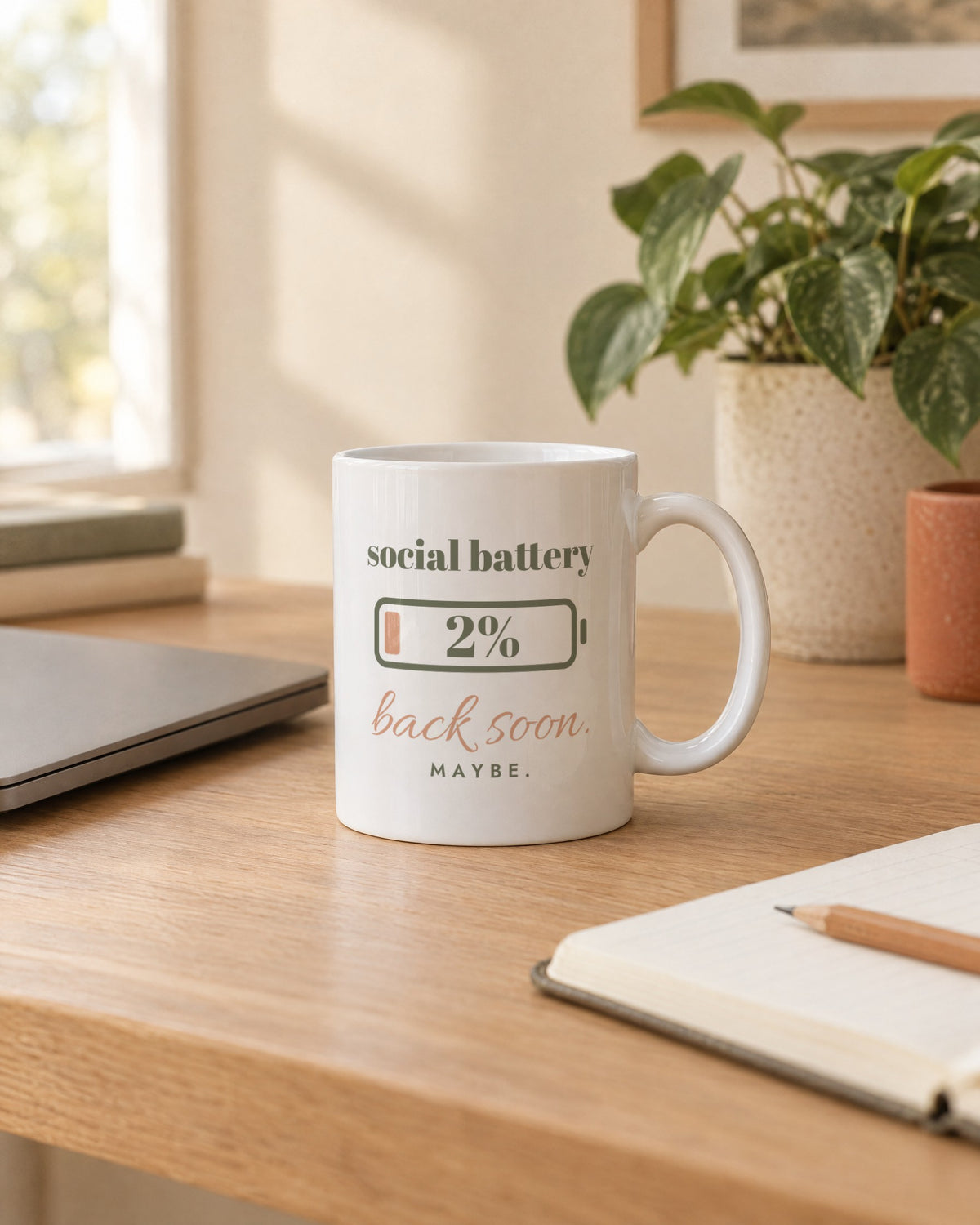 Social Battery Mug, white ceramic 11 oz, on a desk next to a laptop