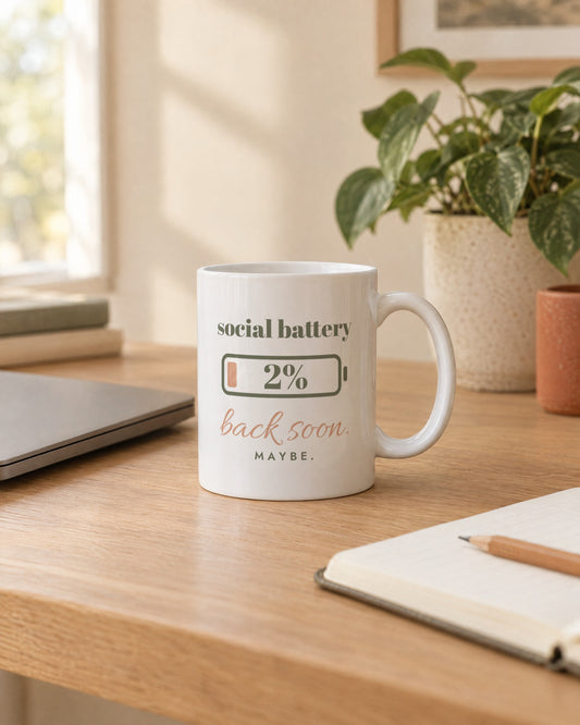 Social Battery Mug, white ceramic 11 oz, on a desk next to a laptop