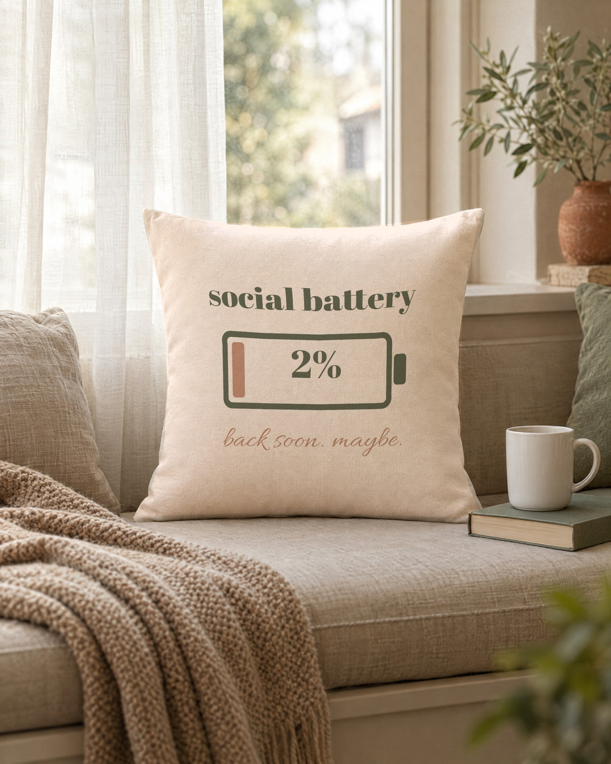 Social Battery Pillow, 18 x 18 in, propped on a window seat