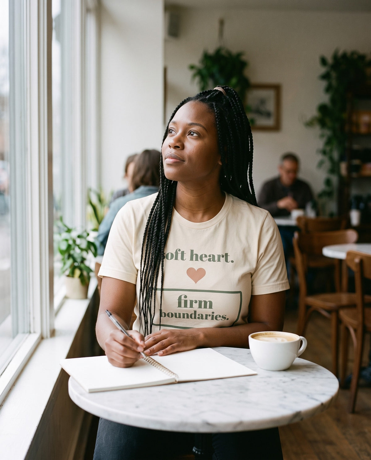 Soft Heart, Firm Boundaries Tee, worn at a cafe table with a notebook