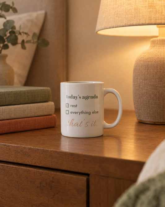 Today's Agenda Mug, white ceramic 11 oz, on a bedside table by a lamp