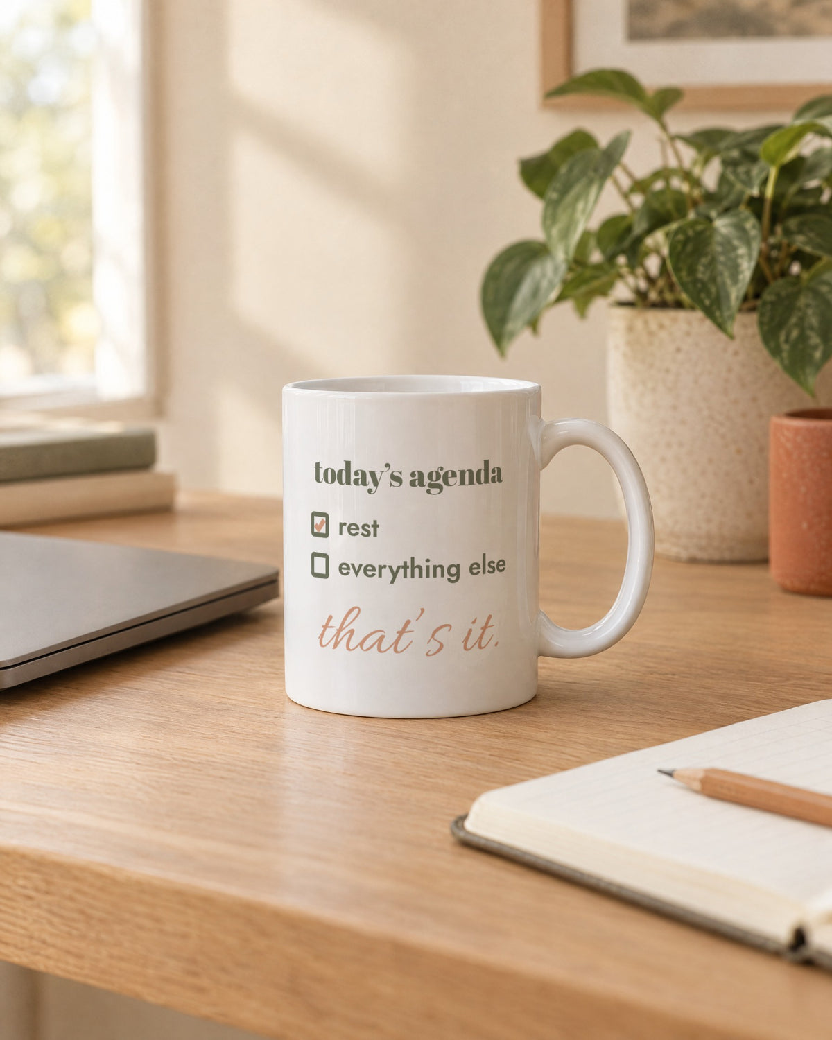 Today's Agenda Mug, white ceramic 11 oz, on a desk next to a laptop